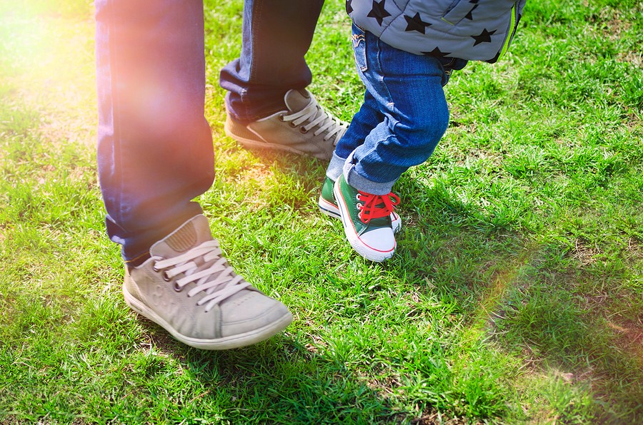 First Steps Concept - Foot Of Father And Son In Stylish Sneakers On The Background Of Green Grass. B
